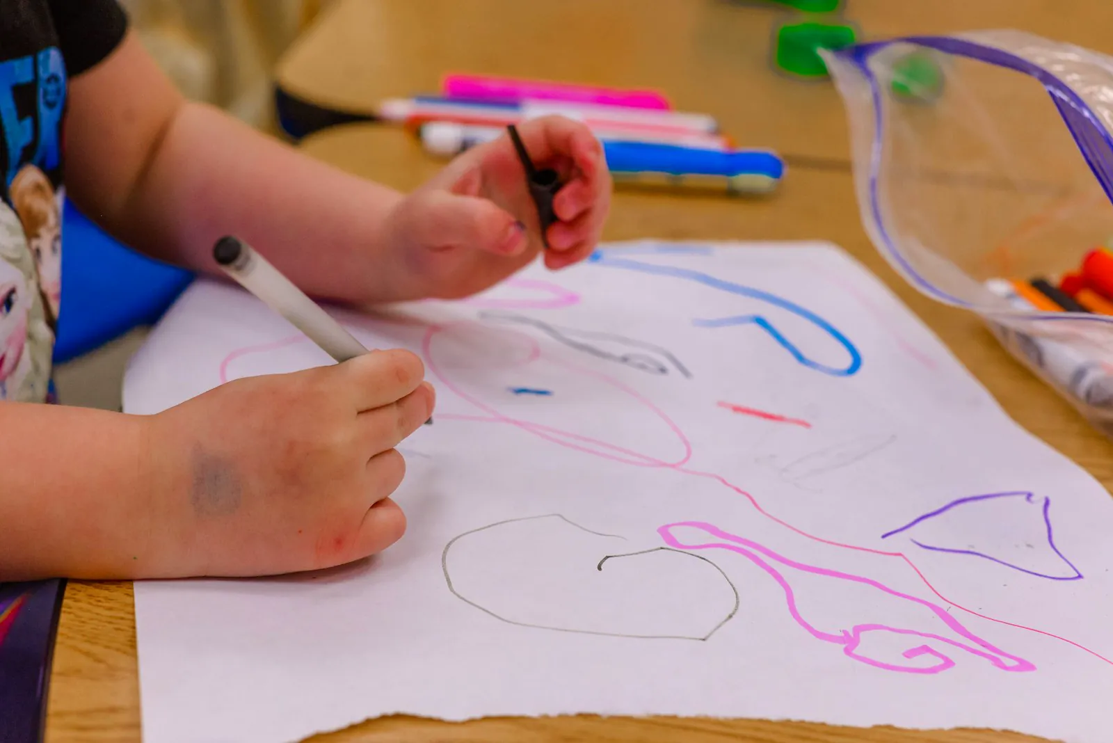 A young child leans over a table, focused on drawing on a sheet of paper.