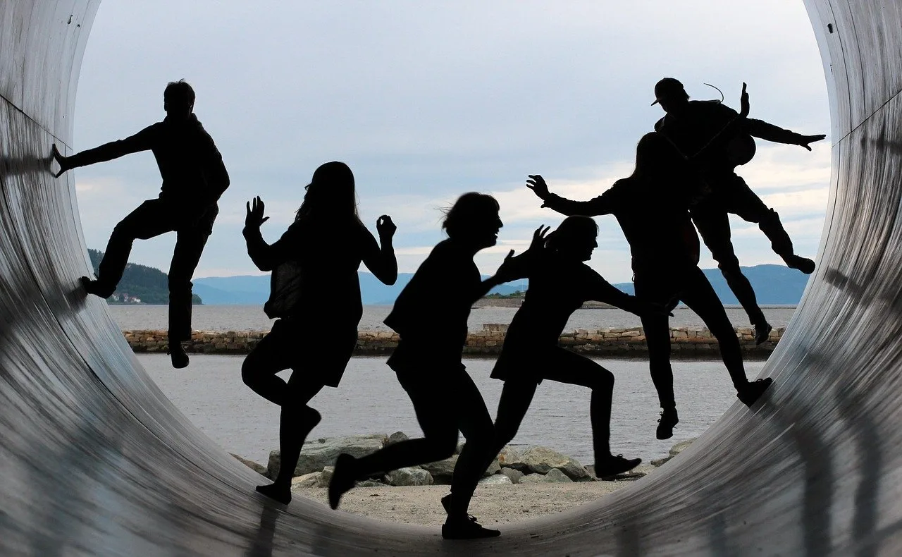 Silhouettes of several friends jumping and posing inside a large tunnel by the water.