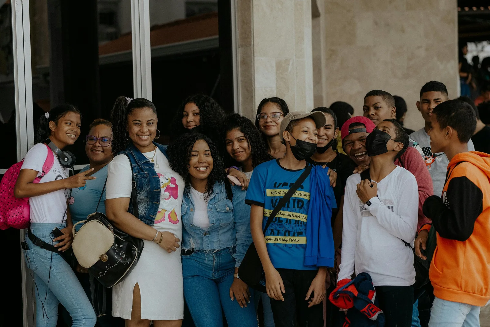 A group of teenagers pose together smiling outside a building entrance.