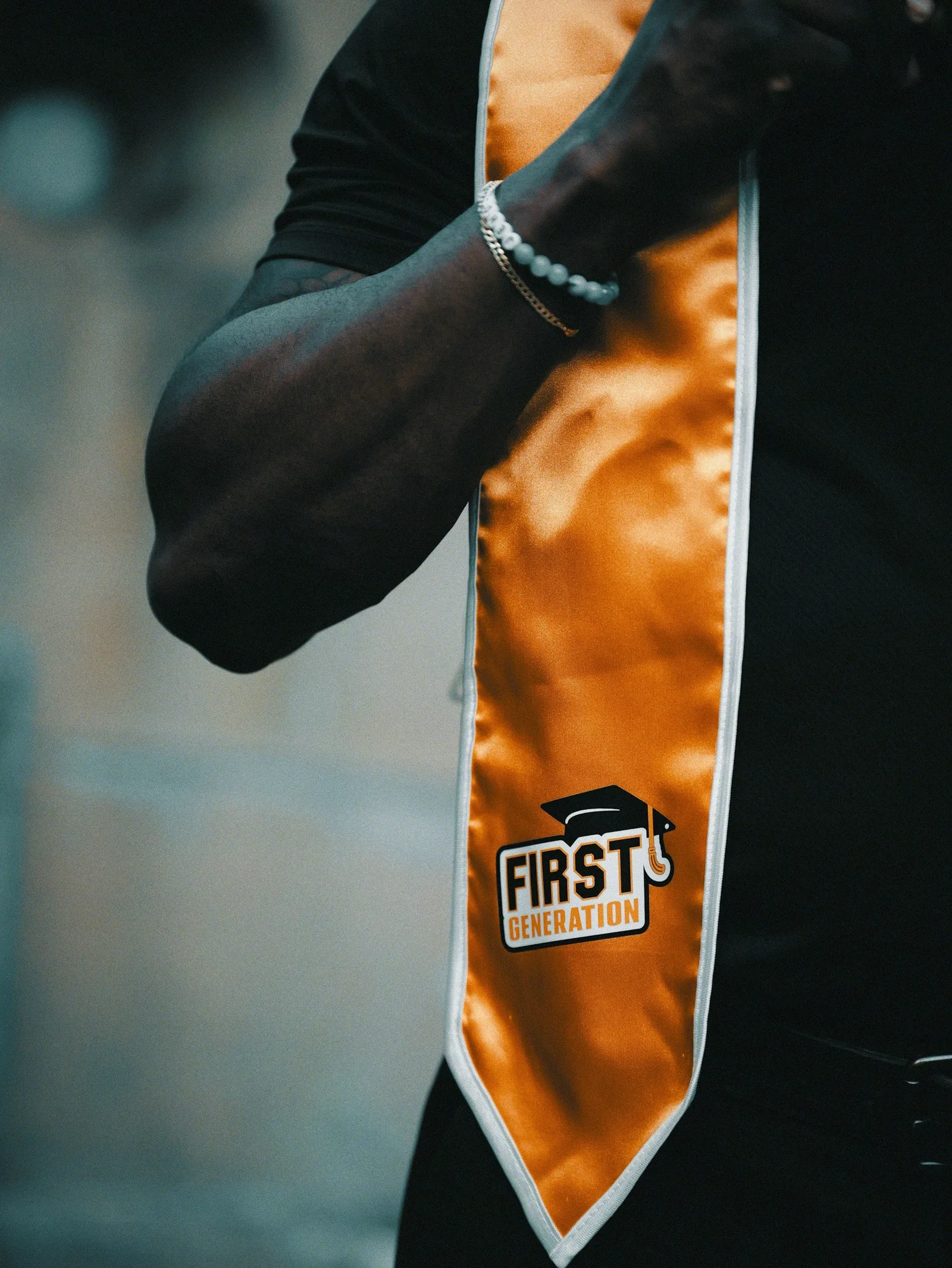 A close-up of an arm wearing a graduation stole reading "First Generation."