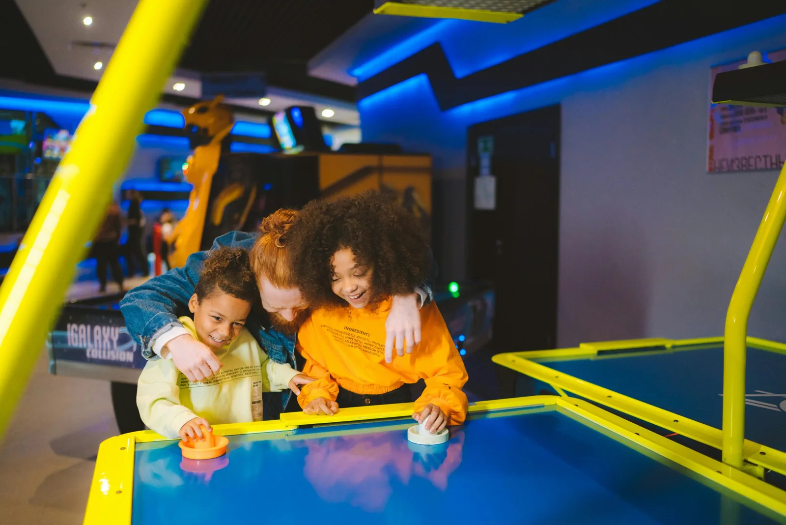 Three children play an arcade air hockey game together.