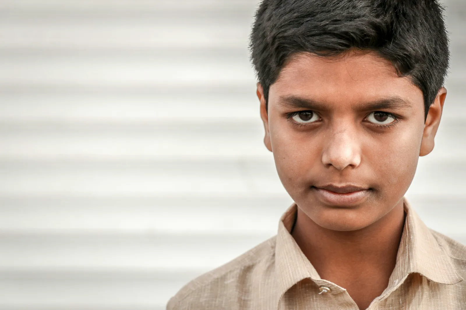 A teenage boy in a beige shirt stands calmly with a gentle, hopeful expression.