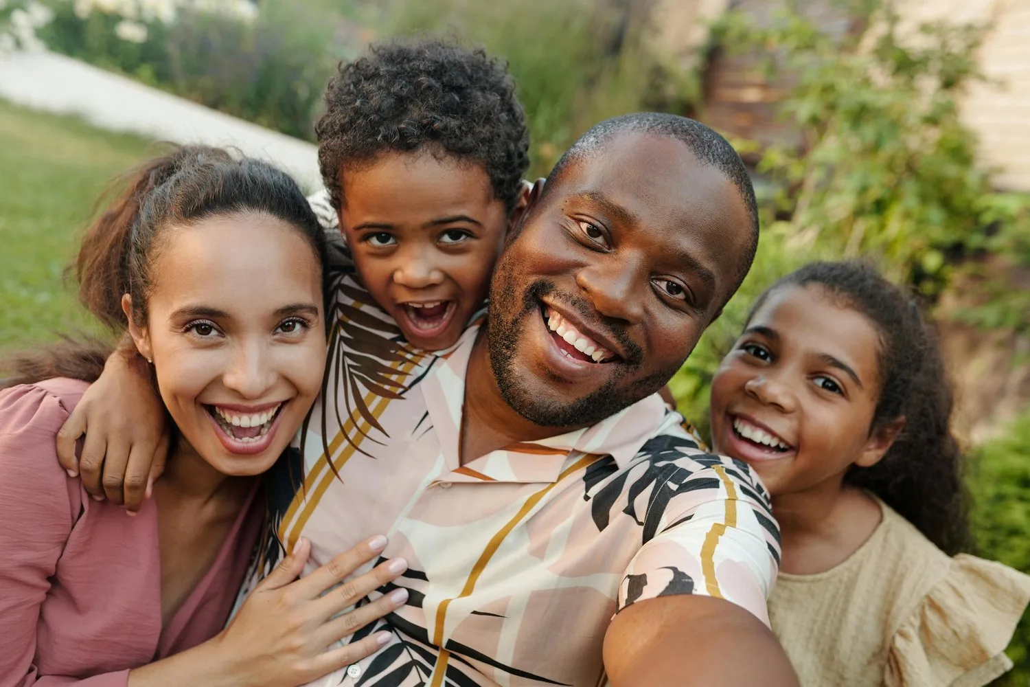 A family of four takes a close-up selfie together outdoors, all smiling.
