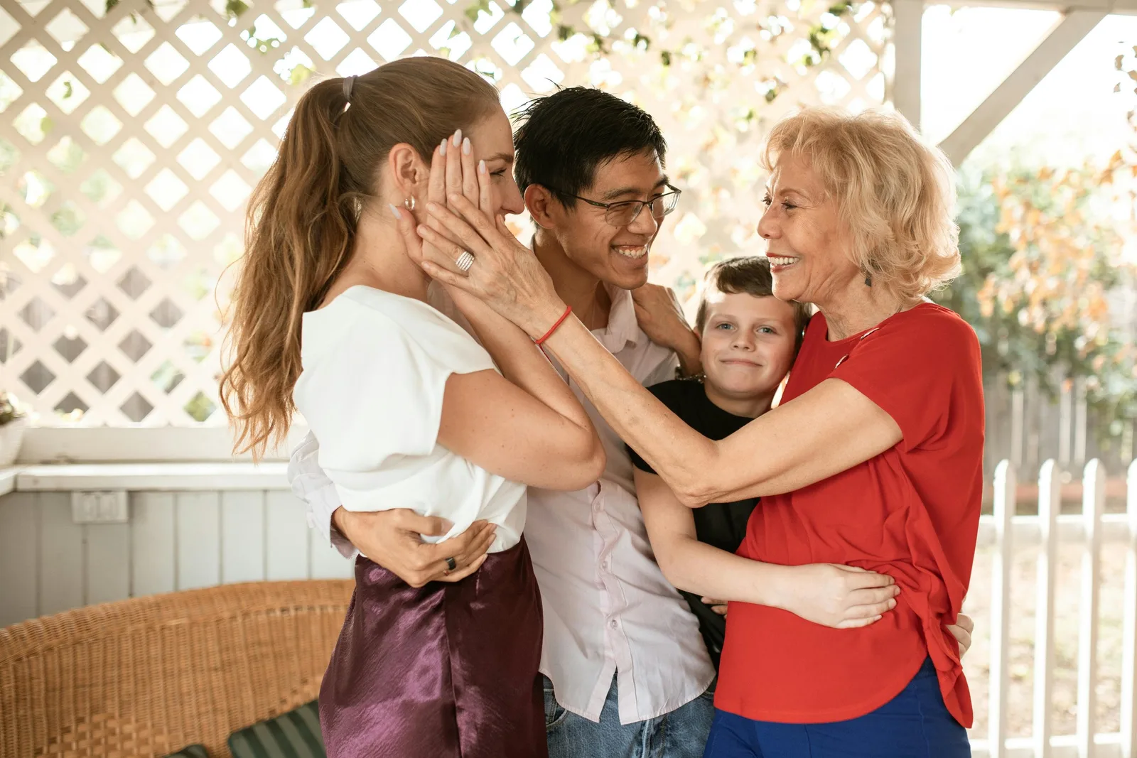 Three generations of a family embrace and laugh together on a porch.