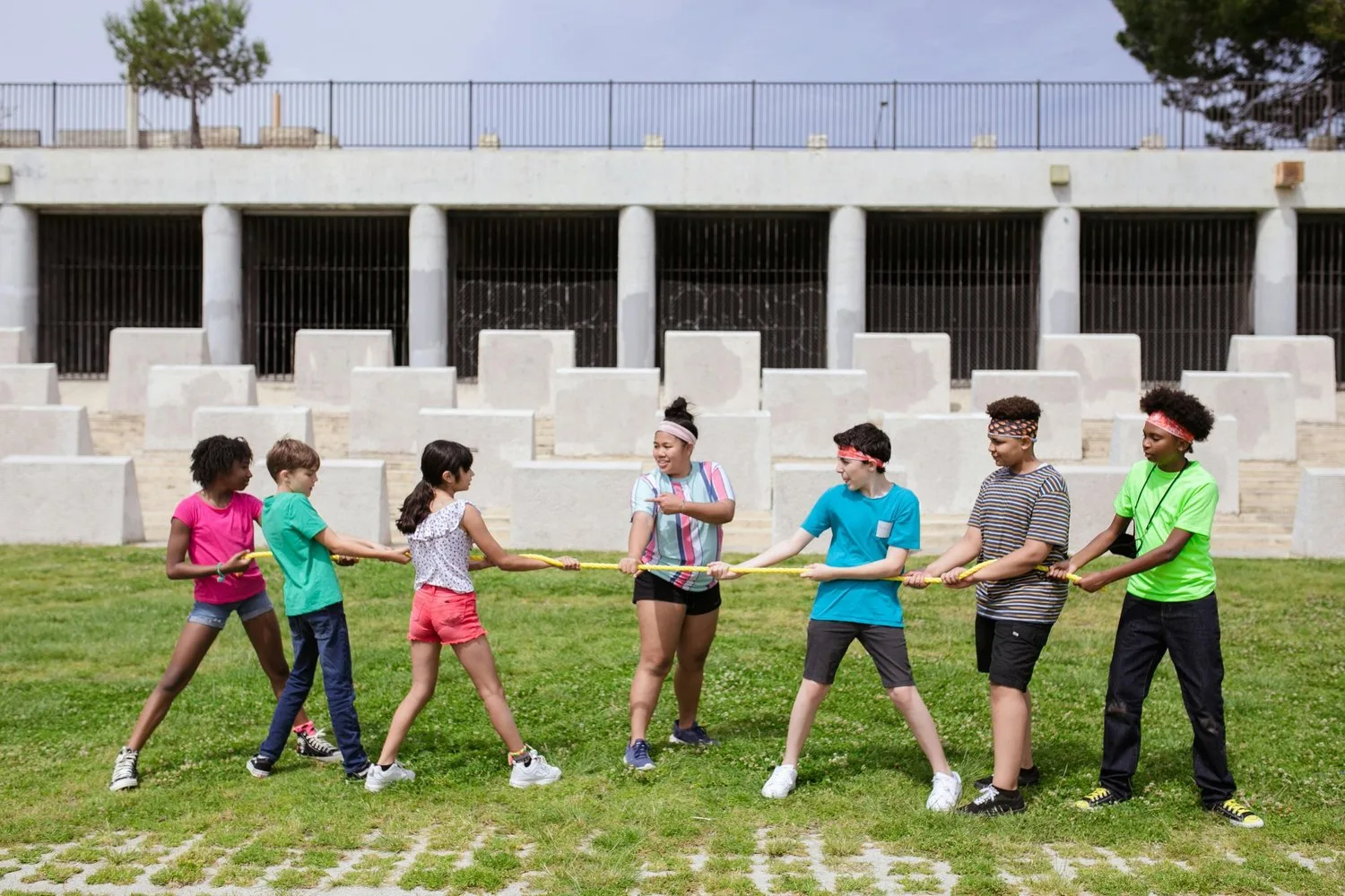 A line of children play tug-of-war with a rope on a grassy field.