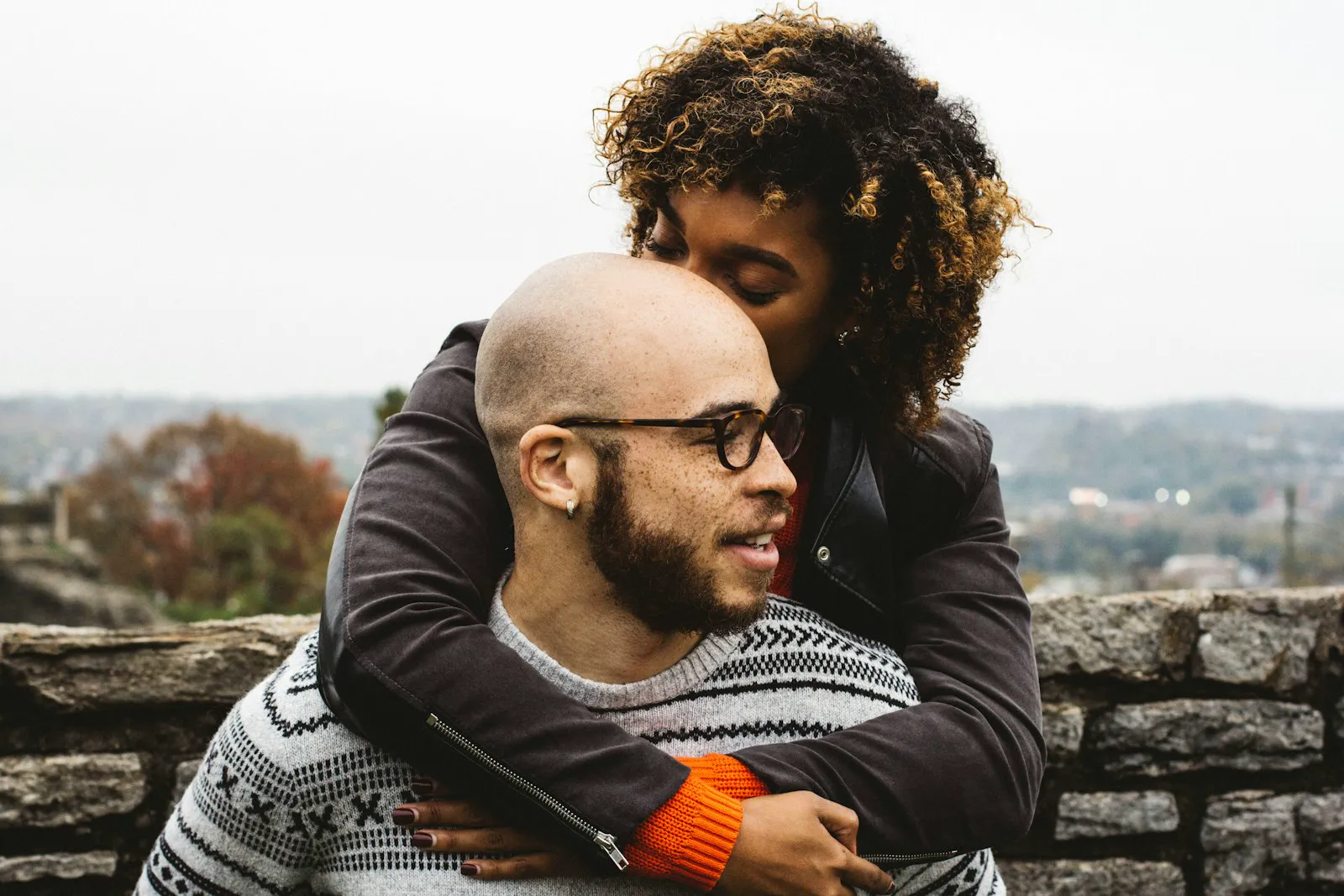 A woman leans in to kiss the top of her partner's head as the two sit close together.