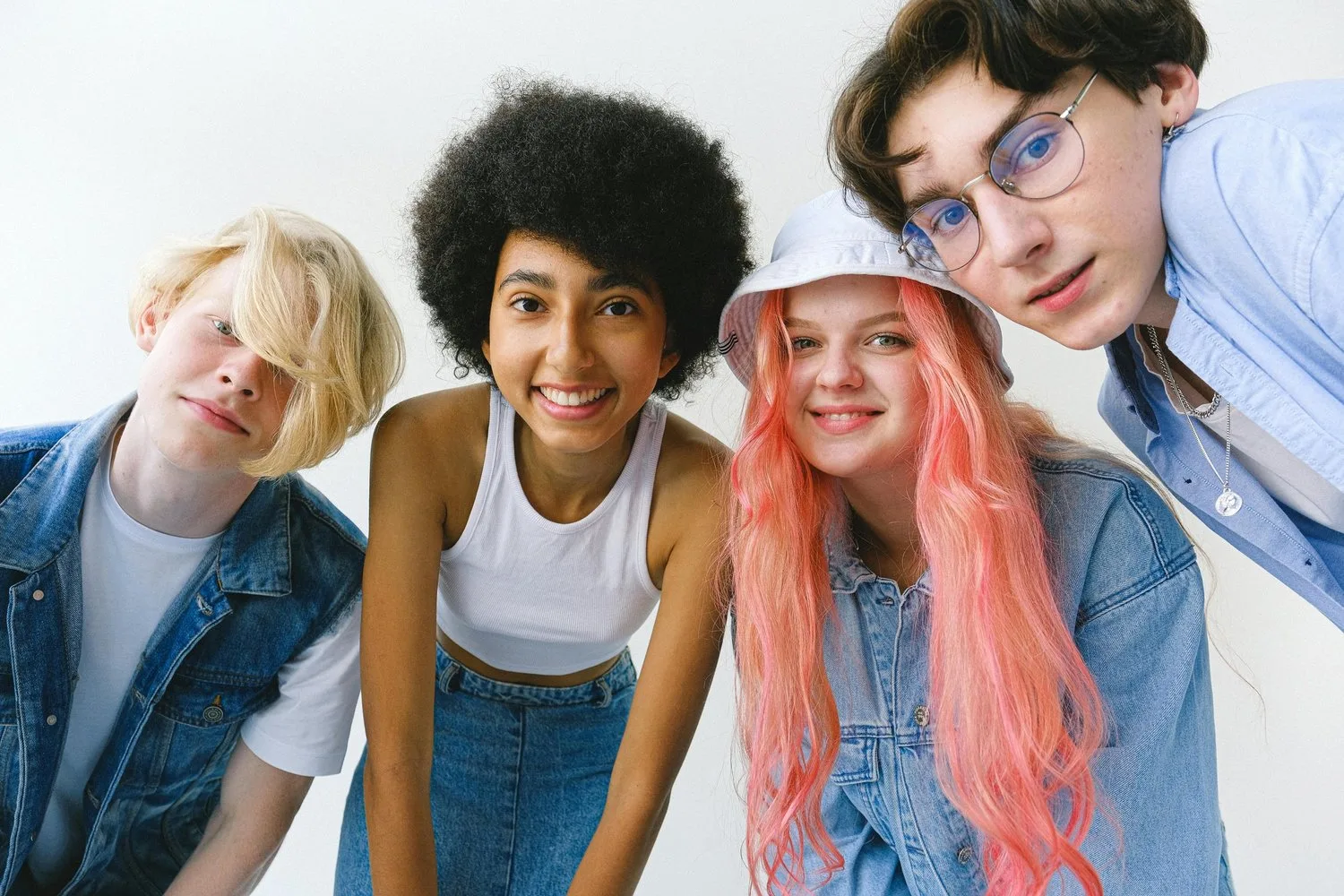 Four teenagers with varied hairstyles lean in close together smiling at the camera.
