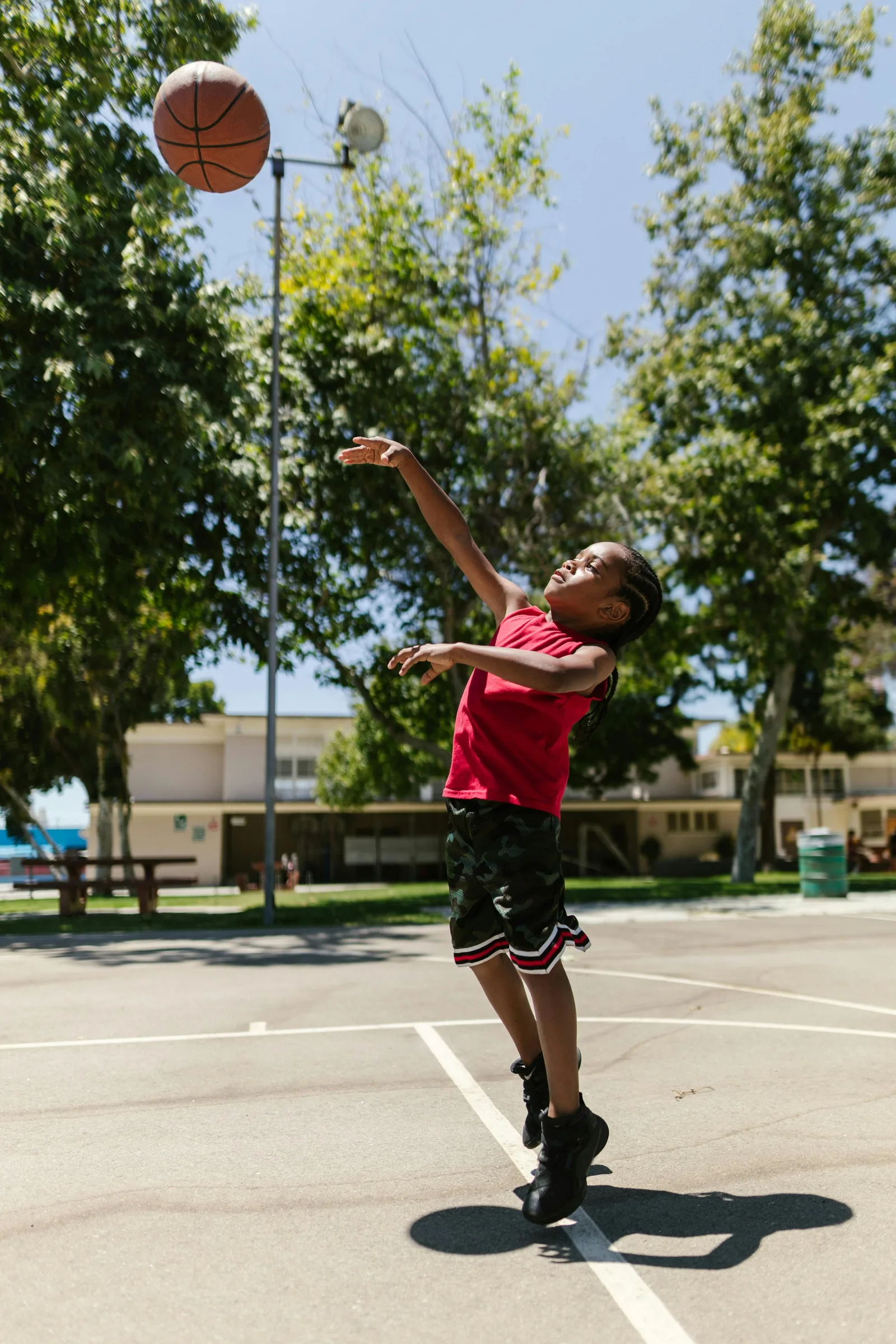 A boy jumps to catch a basketball on an outdoor court.