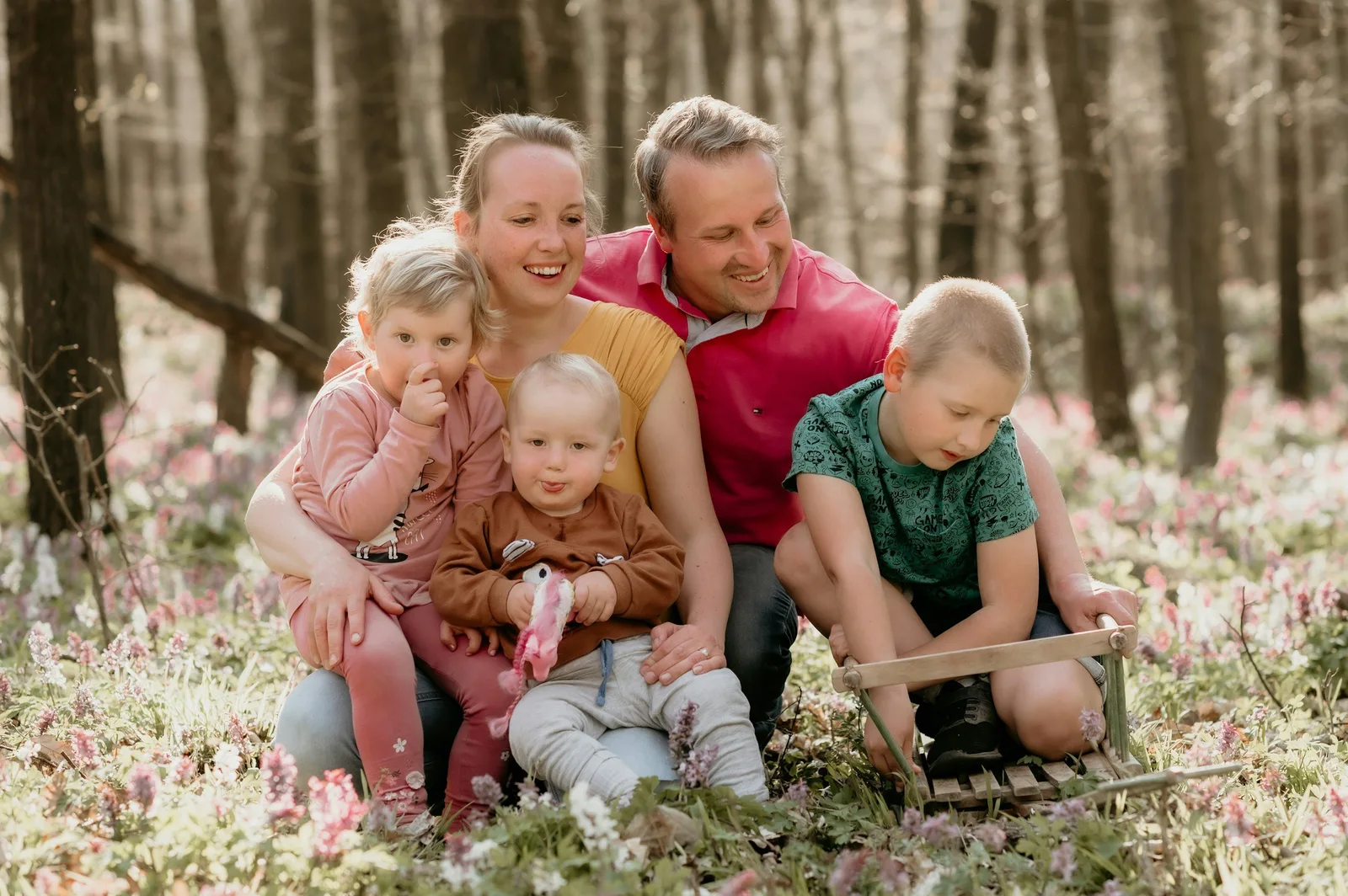A family of five poses together outdoors among trees and spring wildflowers.