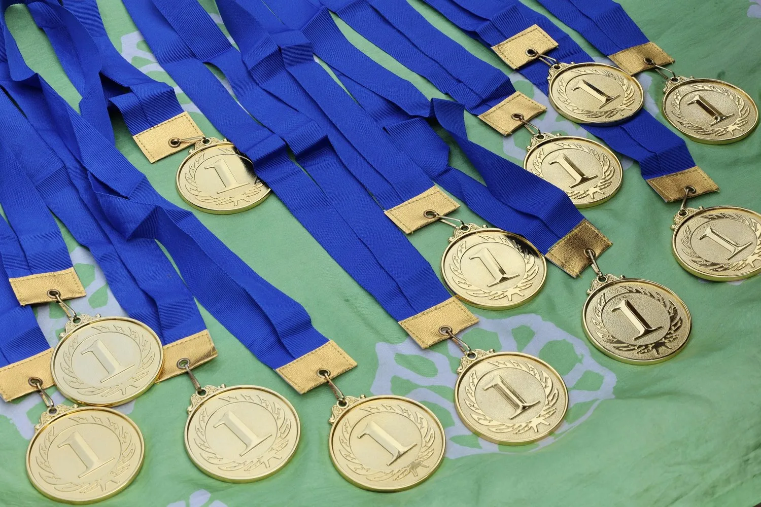 Rows of gold medals with blue ribbons lie on a green cloth.