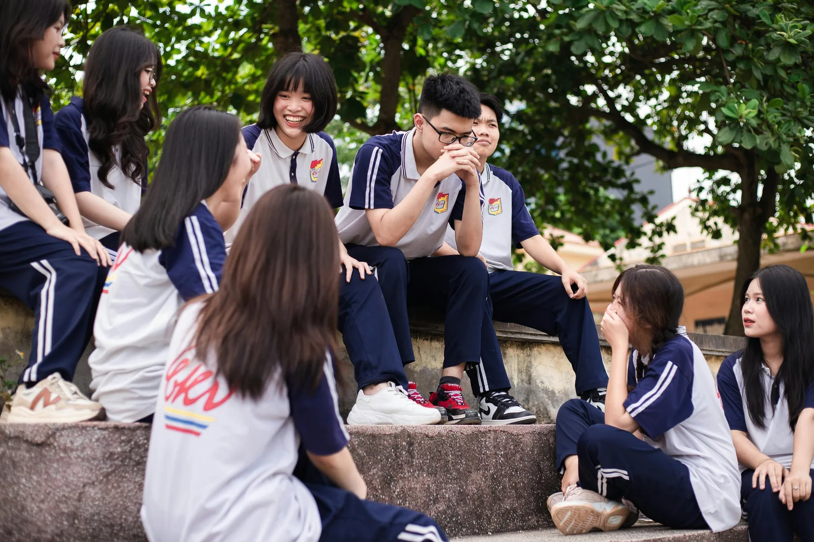 A group of students in matching uniforms sit together on outdoor steps talking and laughing.