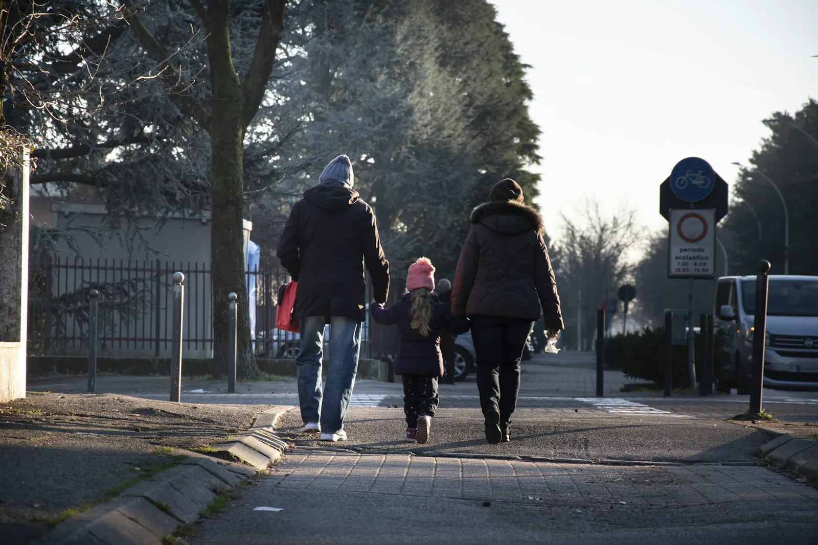 Two parents and a child walk together holding hands along a quiet street.