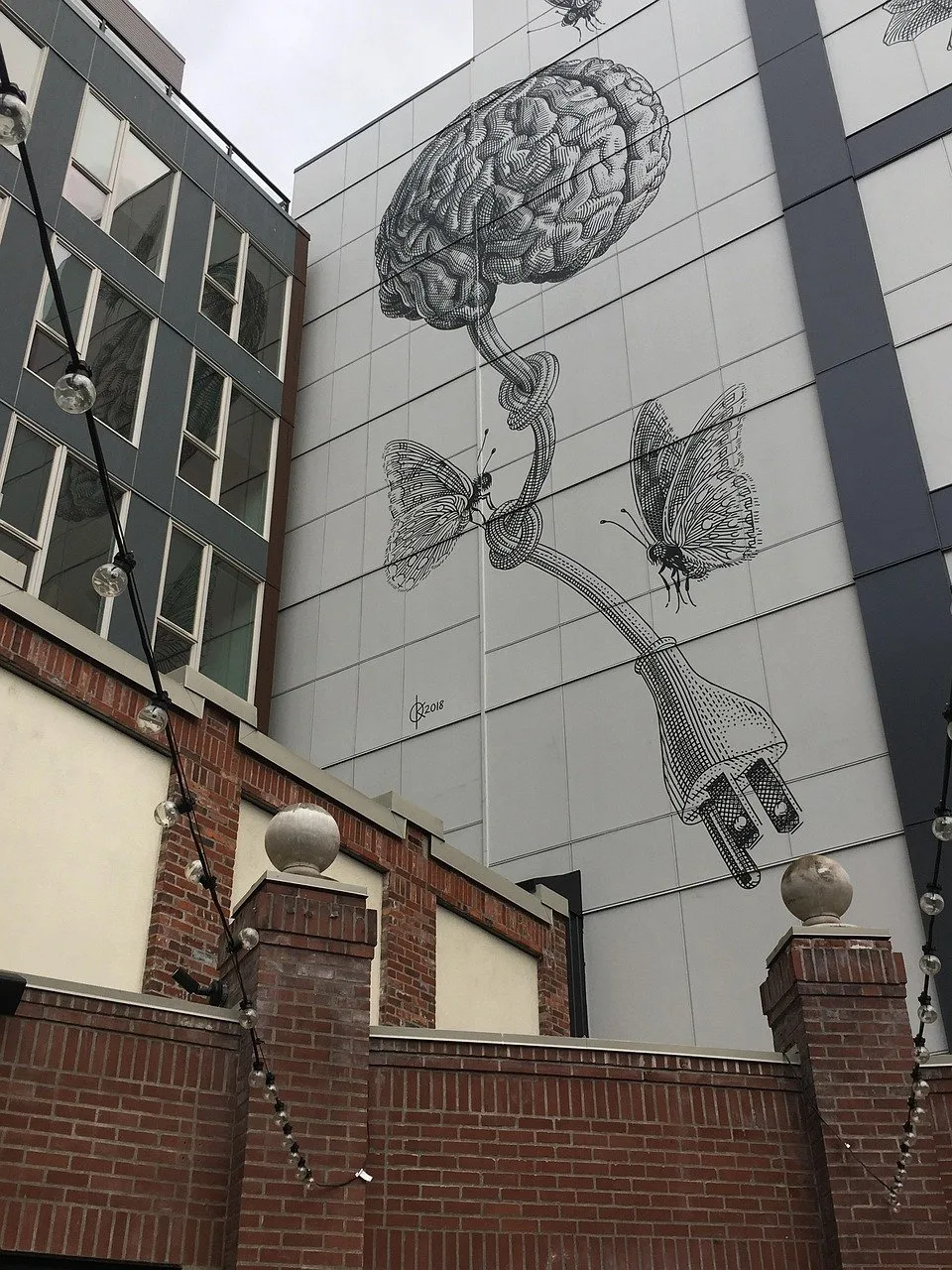 A building mural depicting a large brain connected by a cord to butterflies and an electrical plug.