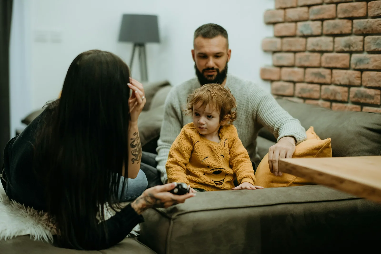 A mother and father sit with a toddler on a couch in a living room.