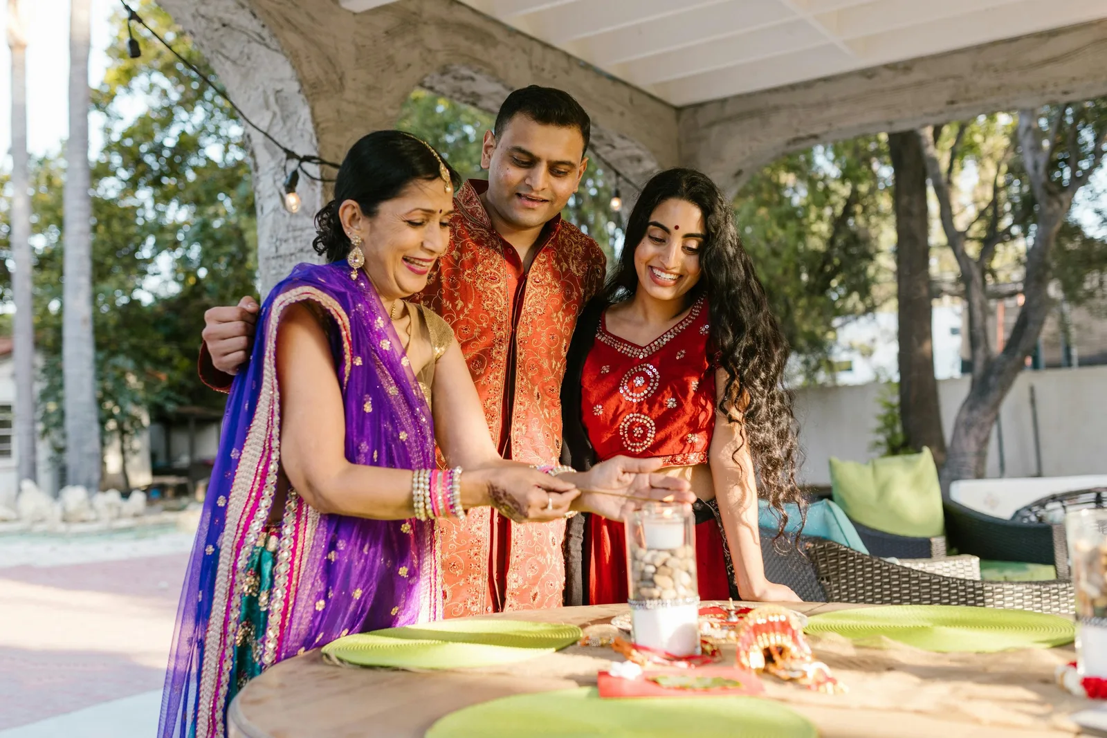 Three people gather around a decorated table during a wedding ceremony, lighting a ceremonial lamp together.