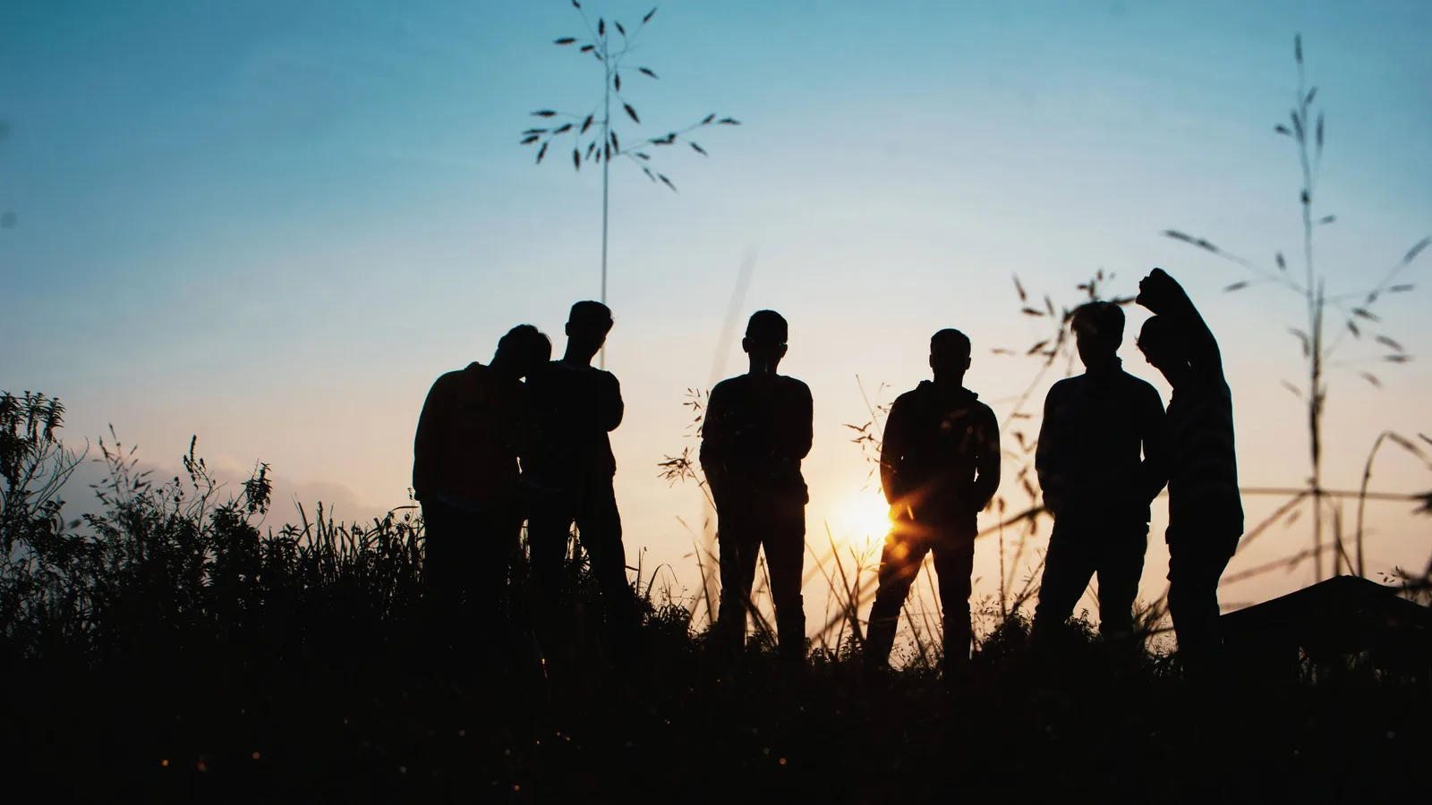 Silhouettes of several people standing together outdoors at sunset.