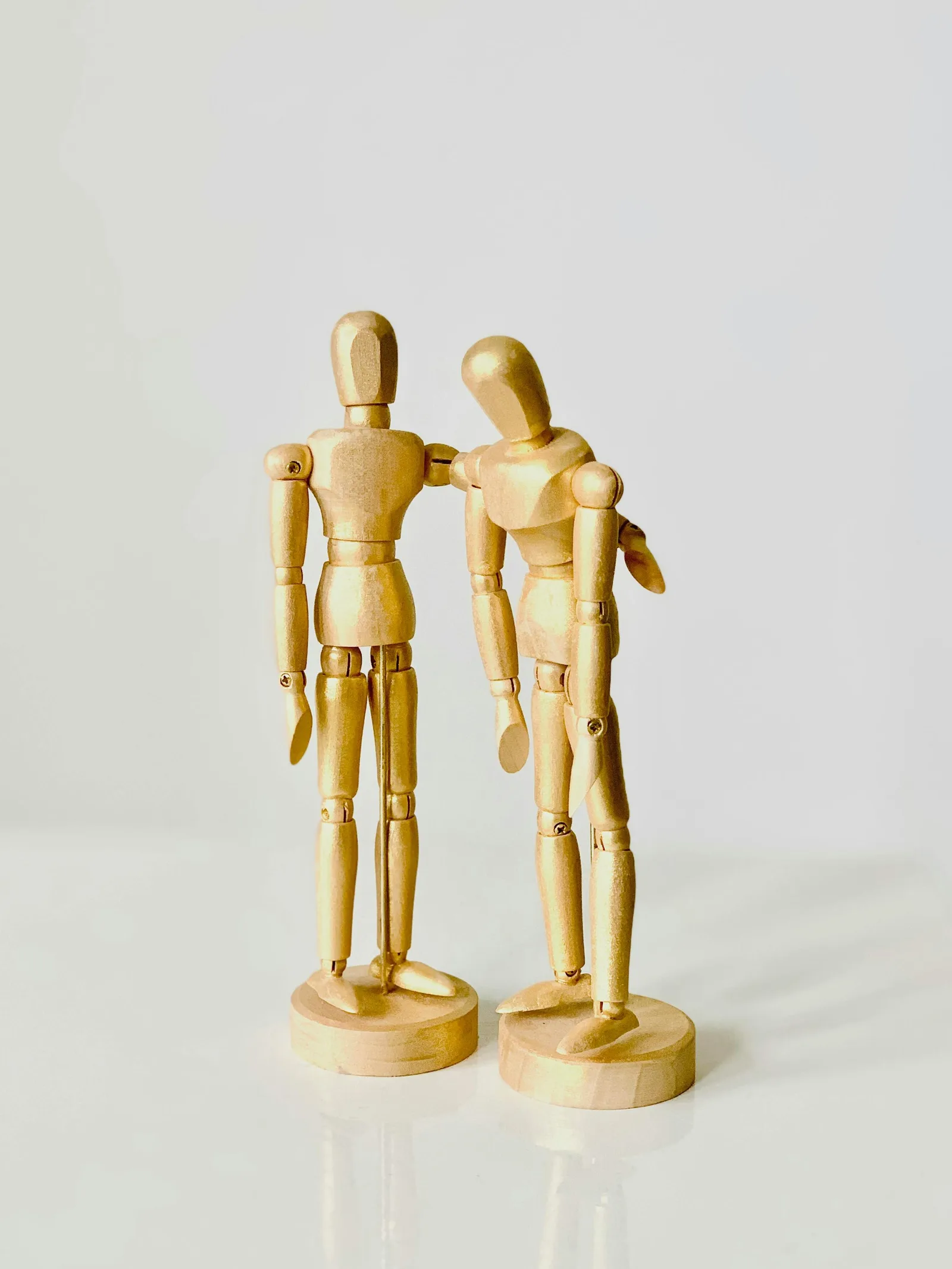 Two wooden artist mannequin figures standing close together as if in conversation.
