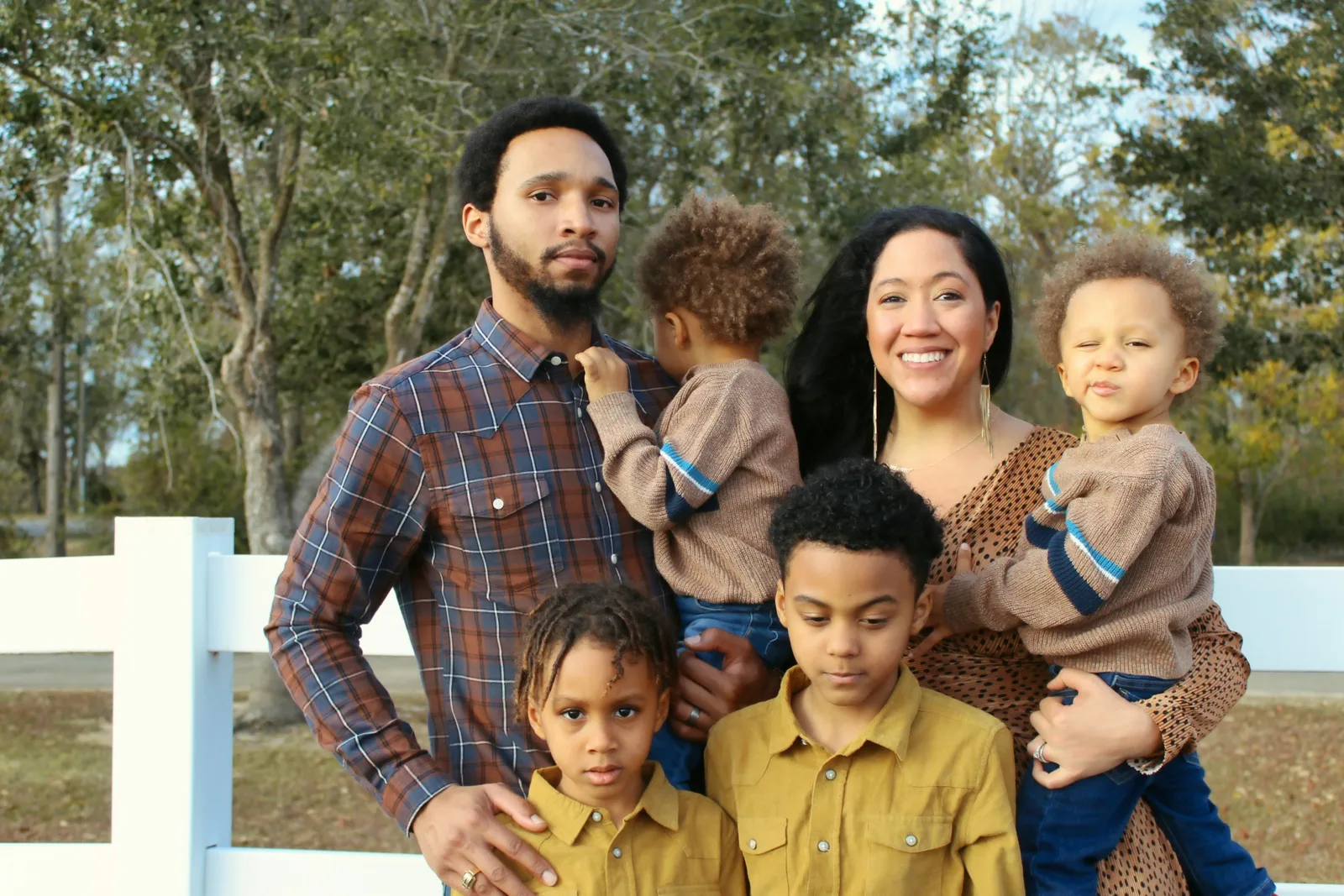 A family of six poses together outdoors in front of a white fence.