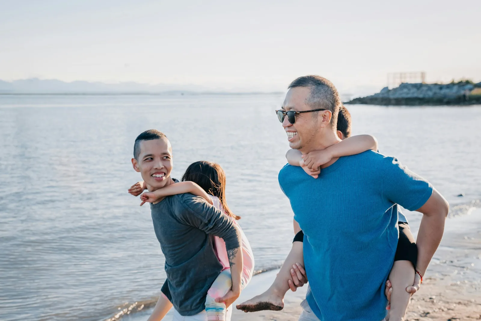 A family plays on a beach at sunset, with a father carrying a child piggyback.