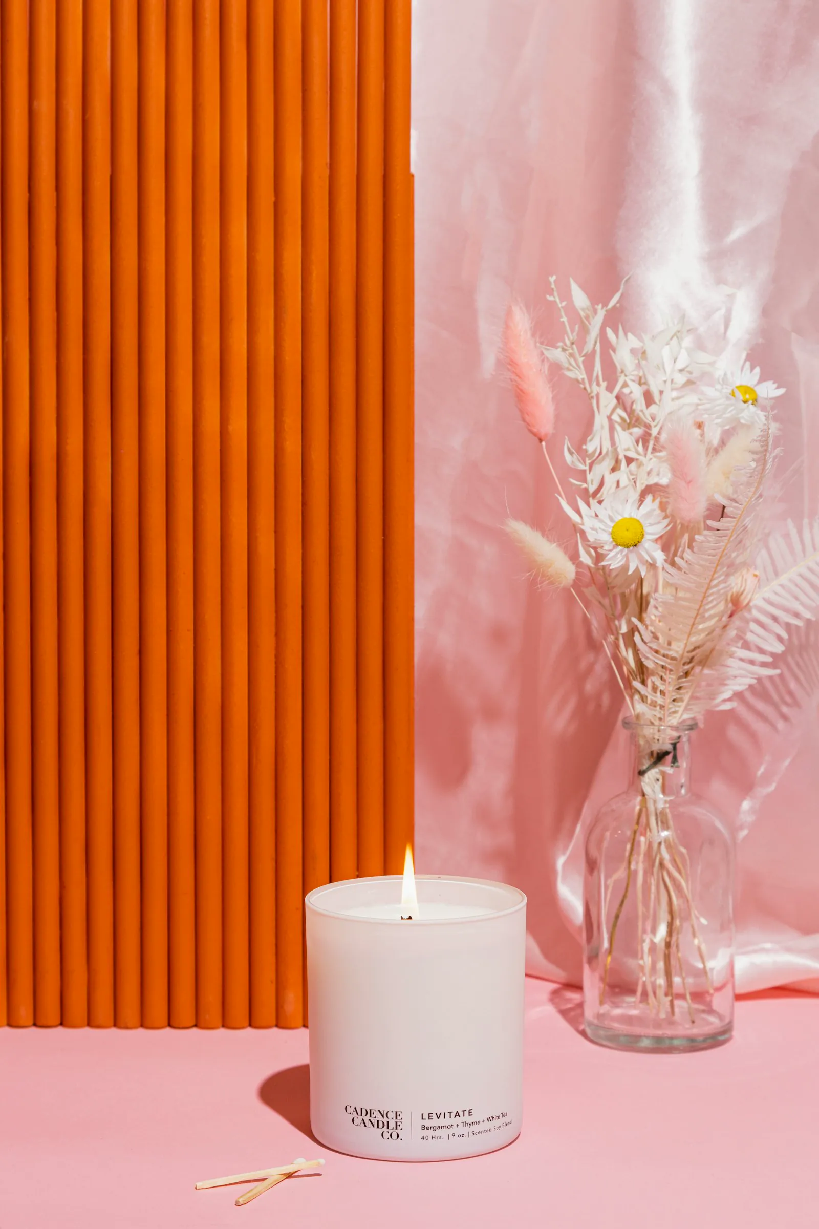 A single white pillar candle glows in a glass holder surrounded by flowers.